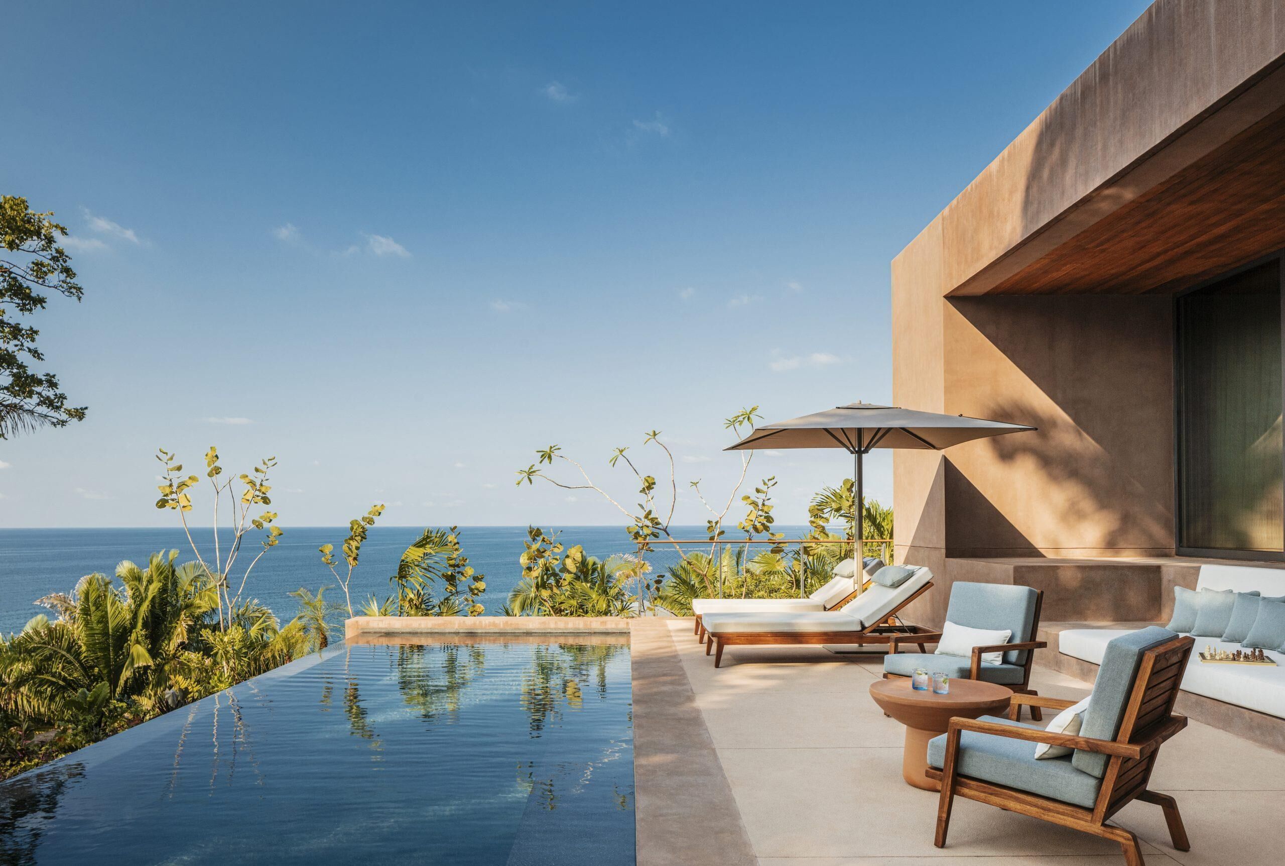 Una piscina infinita con sillones de descanso y una mesa, con vista al océano.