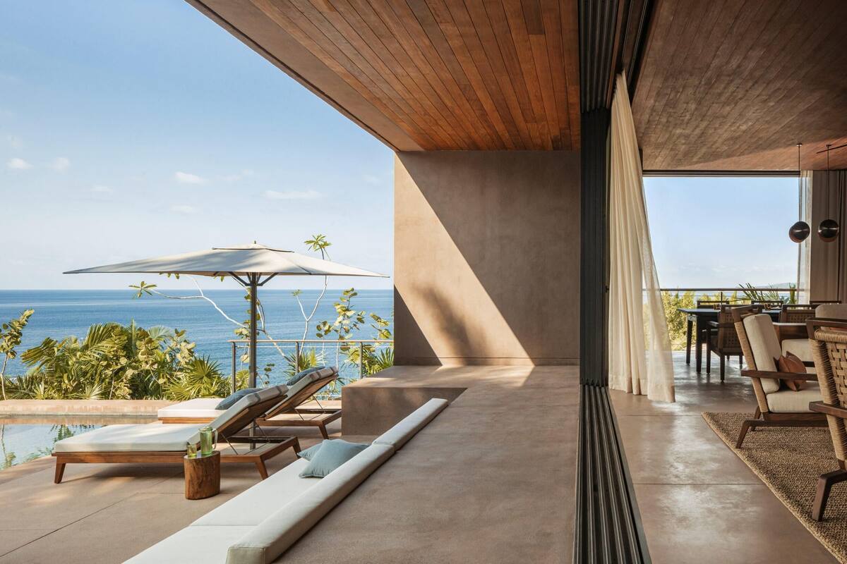 A modern outdoor lounge area with a pool, sun loungers, and a view of the ocean.