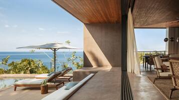 A modern outdoor lounge area with a pool, sun loungers, and a view of the ocean.