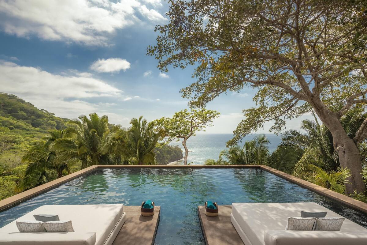 A pool with two lounge chairs and a view of the ocean.