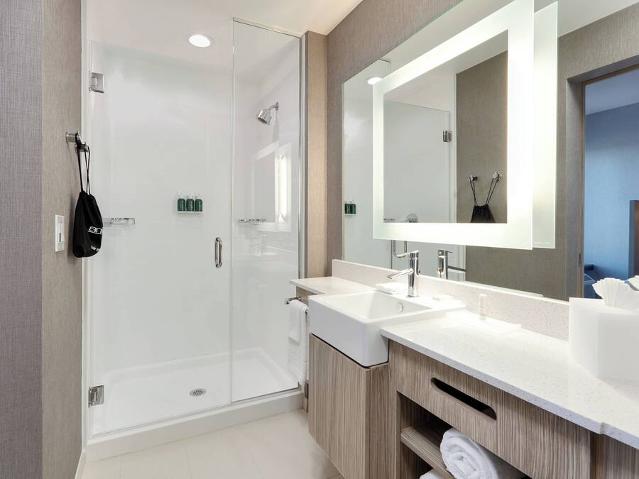 A modern bathroom with a glass-enclosed shower, two sinks, a large mirror, and wooden cabinetry.