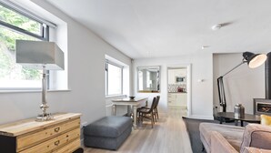 A modern living room with a wooden dresser, a grey ottoman, a sofa, and a dining area with a table and chairs. - The Edge Suite - hiphipstay (Dublin)