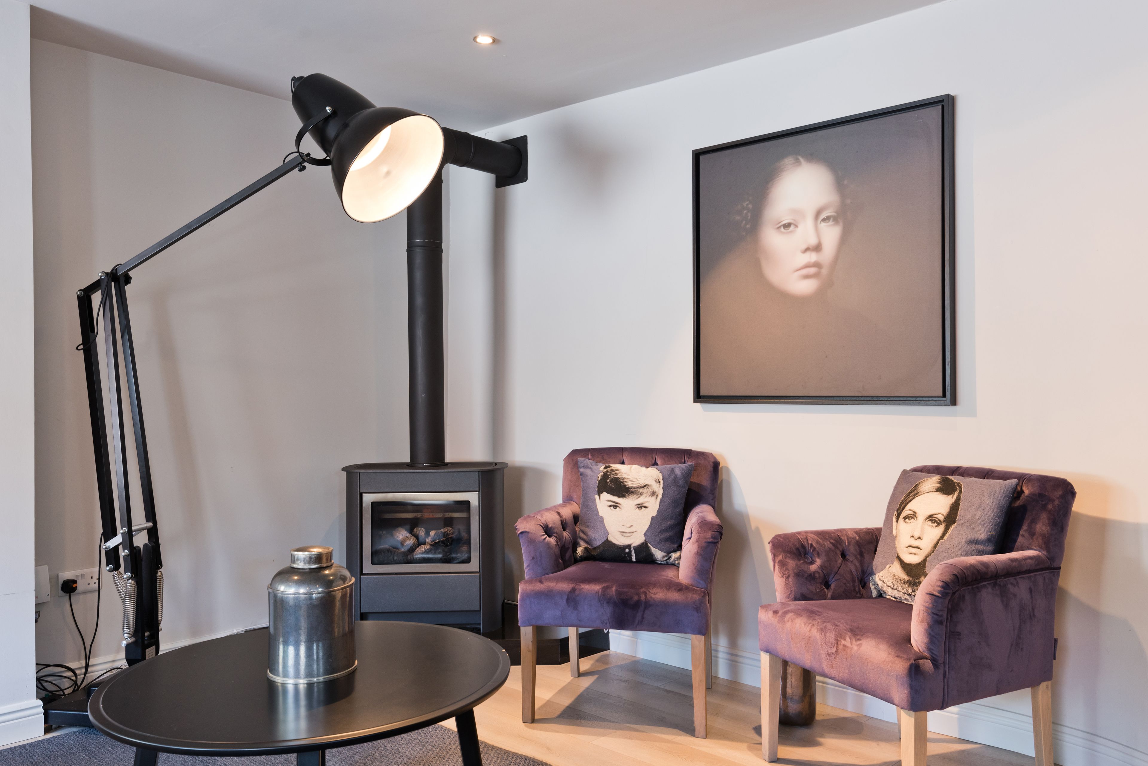 A modern living room with a black floor lamp, a round table, a sofa with a cushion, and a framed portrait on the wall.