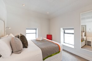 A modern hotel room with a large bed, two windows, a red chair, and a mirror on the wall. - The Edge Suite - hiphipstay (Dublin)