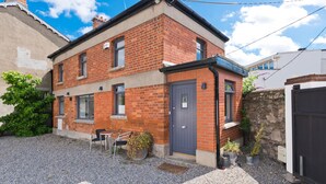 A two-story brick house with a grey door, a small porch with a chair, and potted plants. - The Edge Suite - hiphipstay (Dublin)