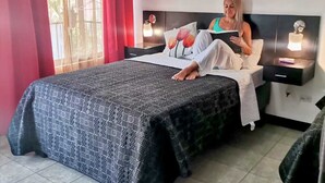 Ein Schlafzimmer mit Bett, Nachttisch, Leselampe und einem Fenster mit Vorhängen.