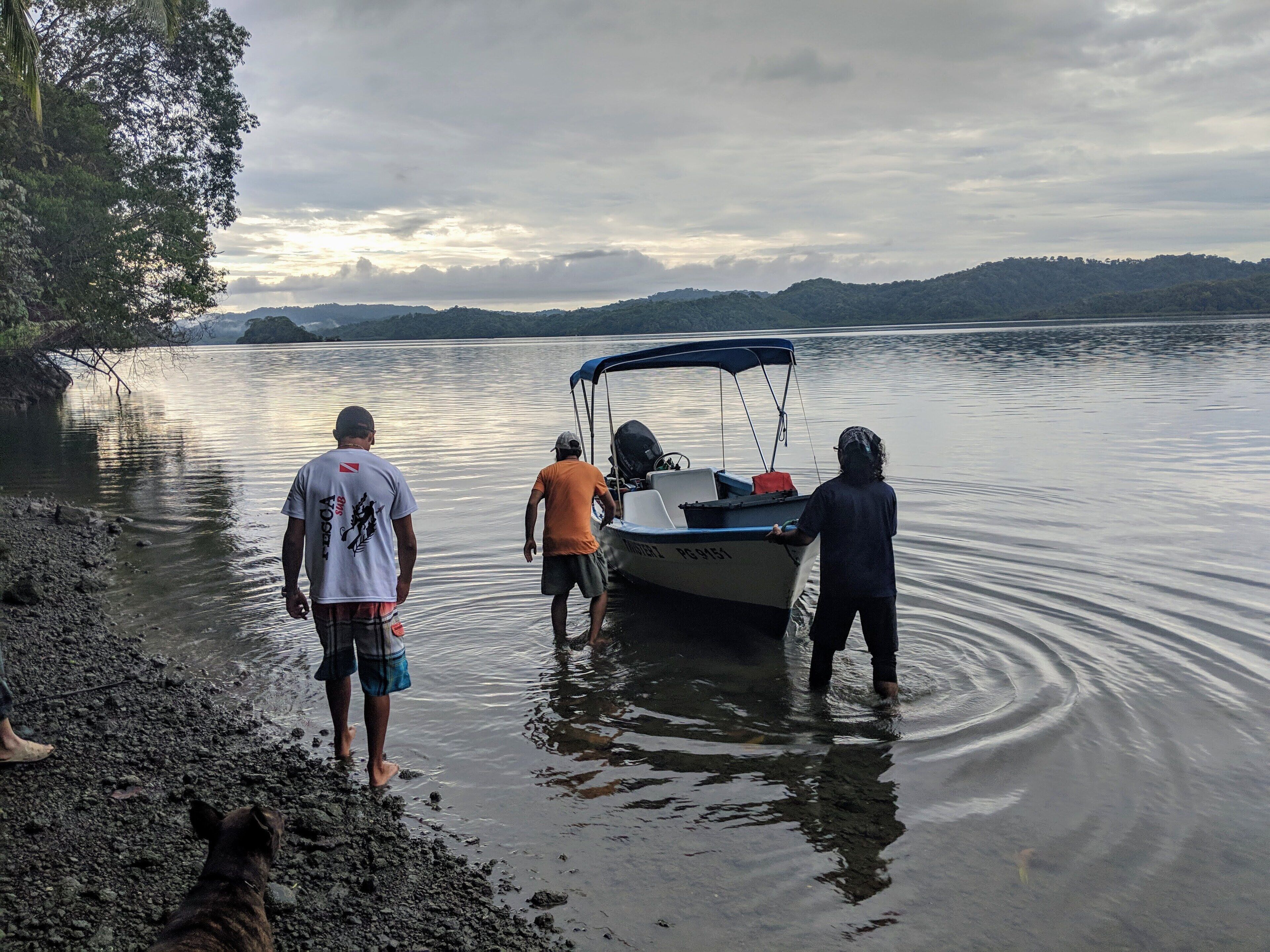 A boat on calm water with people standing at the shore.