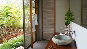 A modern bathroom with a stone sink, a wooden vanity, and a glass shower enclosure. - Cielo Lodge (Golfito)