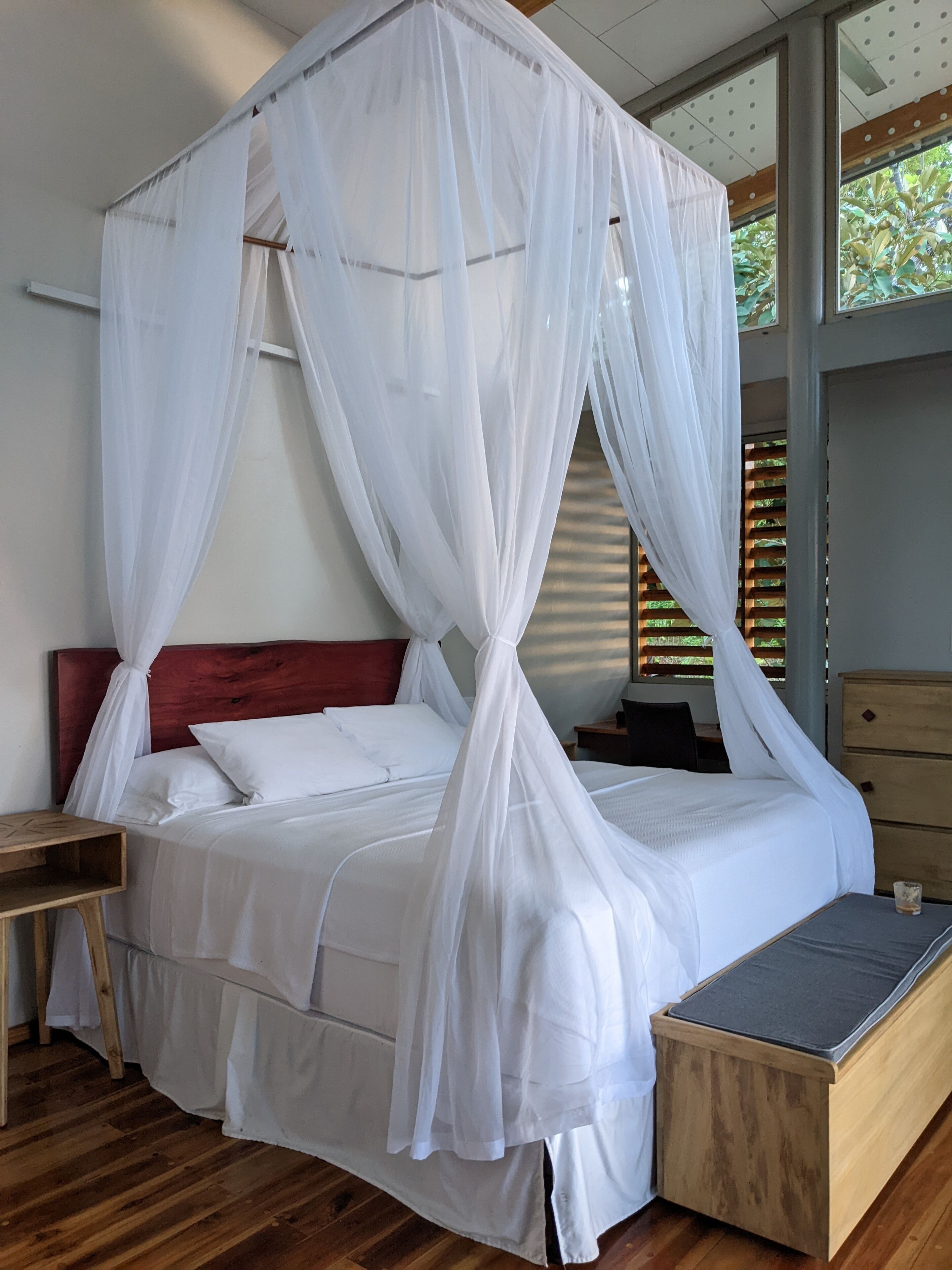 Een hemelbed met witte beddengoed, een houten hoofdbord en een nachtkastje.