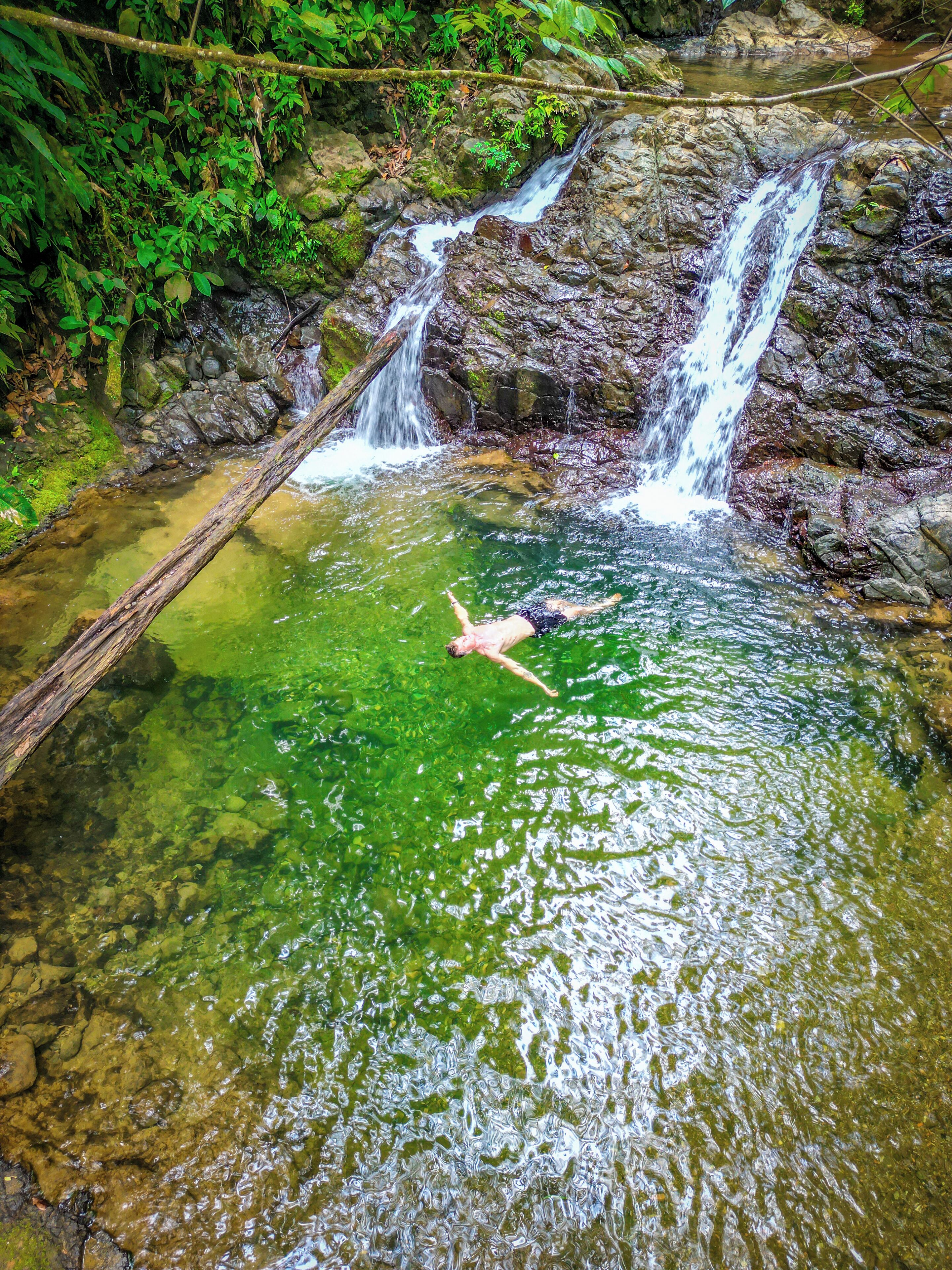 A clear water body with a person swimming, surrounded by rocks and greenery.