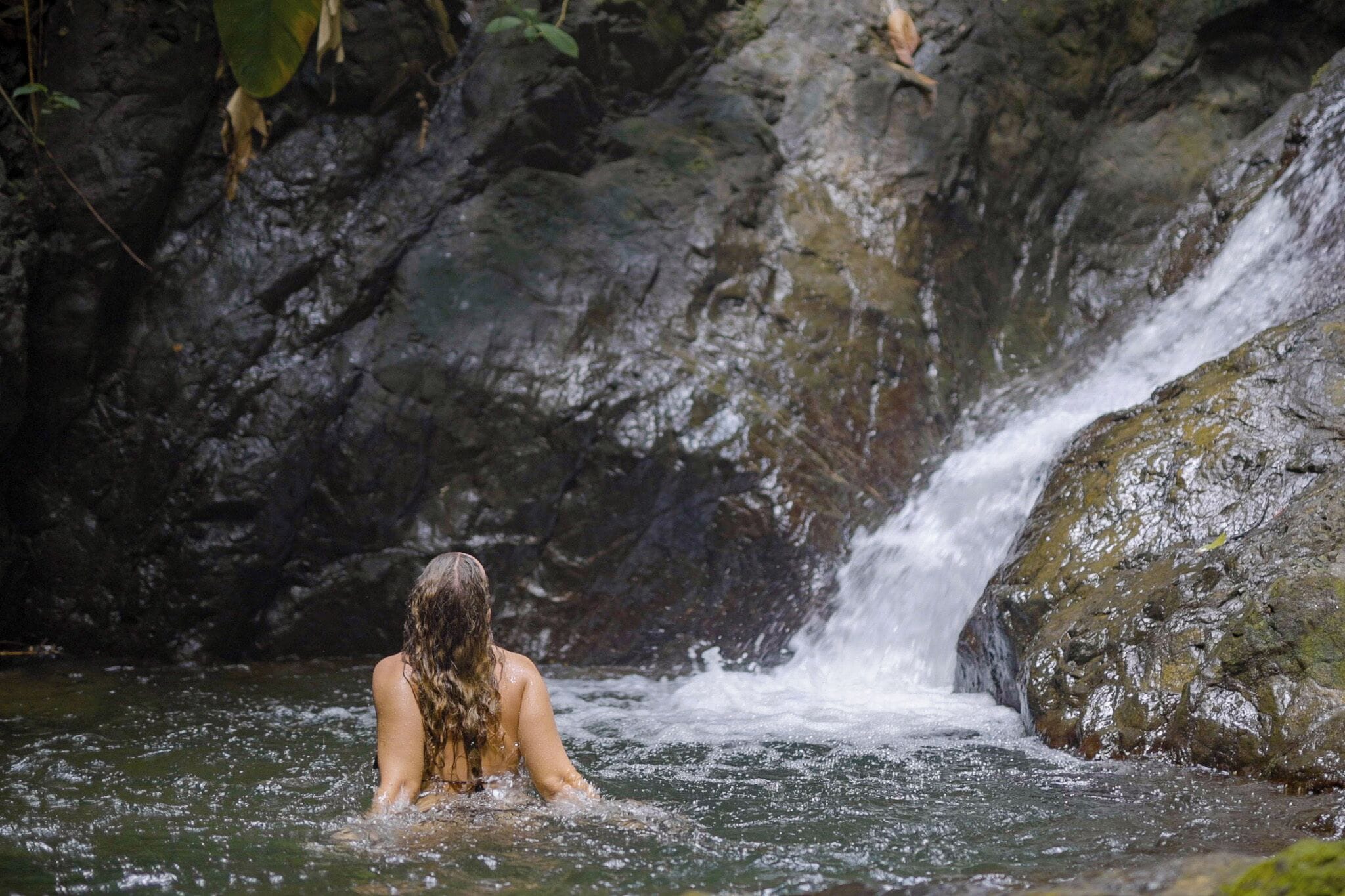 A person in a natural water setting with a waterfall and rocky terrain.