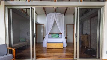 A bedroom with a canopy bed, sliding glass doors, and a wooden floor.