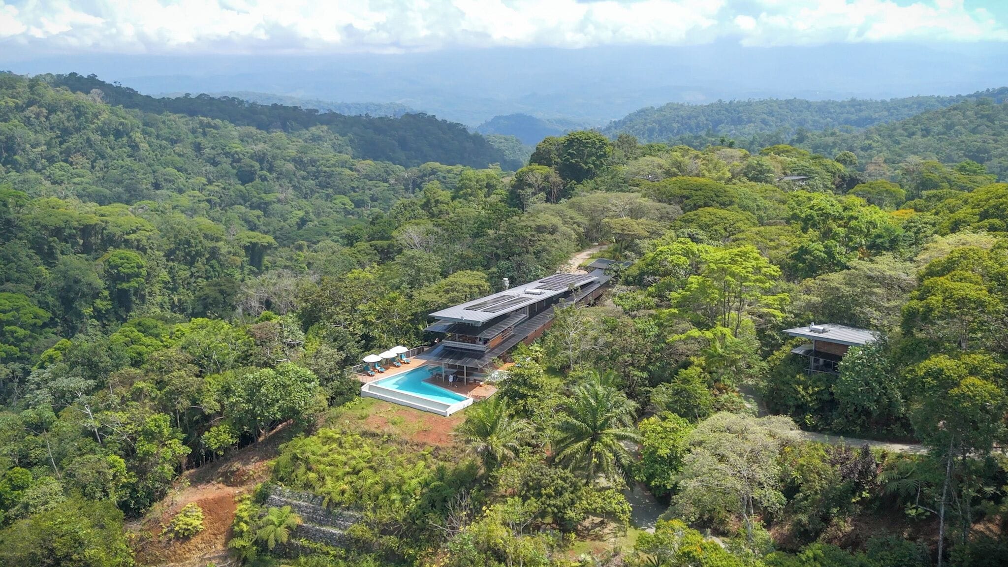 A resort with a swimming pool surrounded by lush greenery and hills in the background.