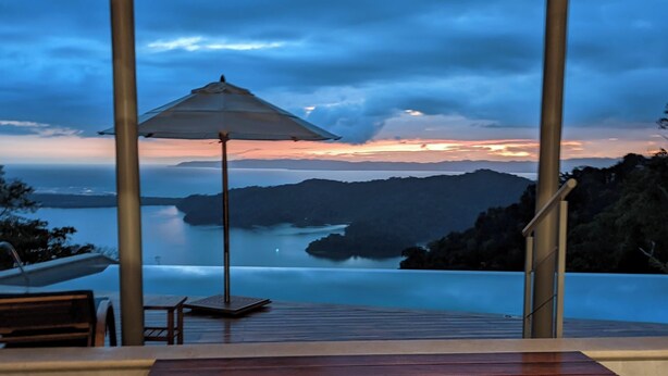 A view from an infinity pool overlooking a body of water with a sunset in the background. - Cielo Lodge (Golfito)