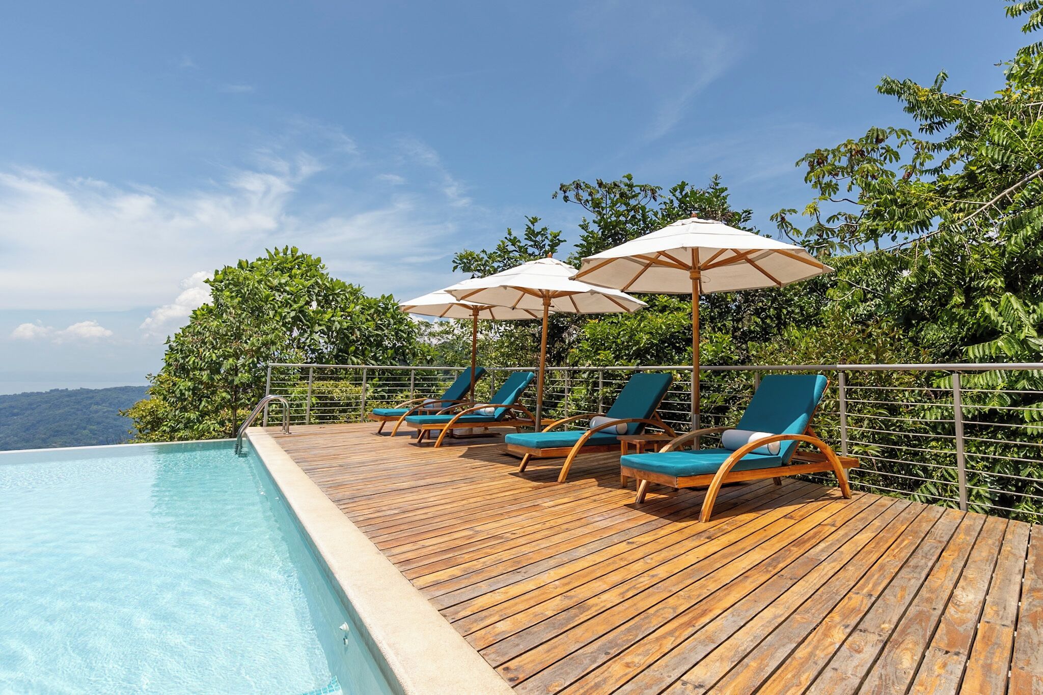A wooden deck with lounge chairs and umbrellas overlooking a swimming pool.