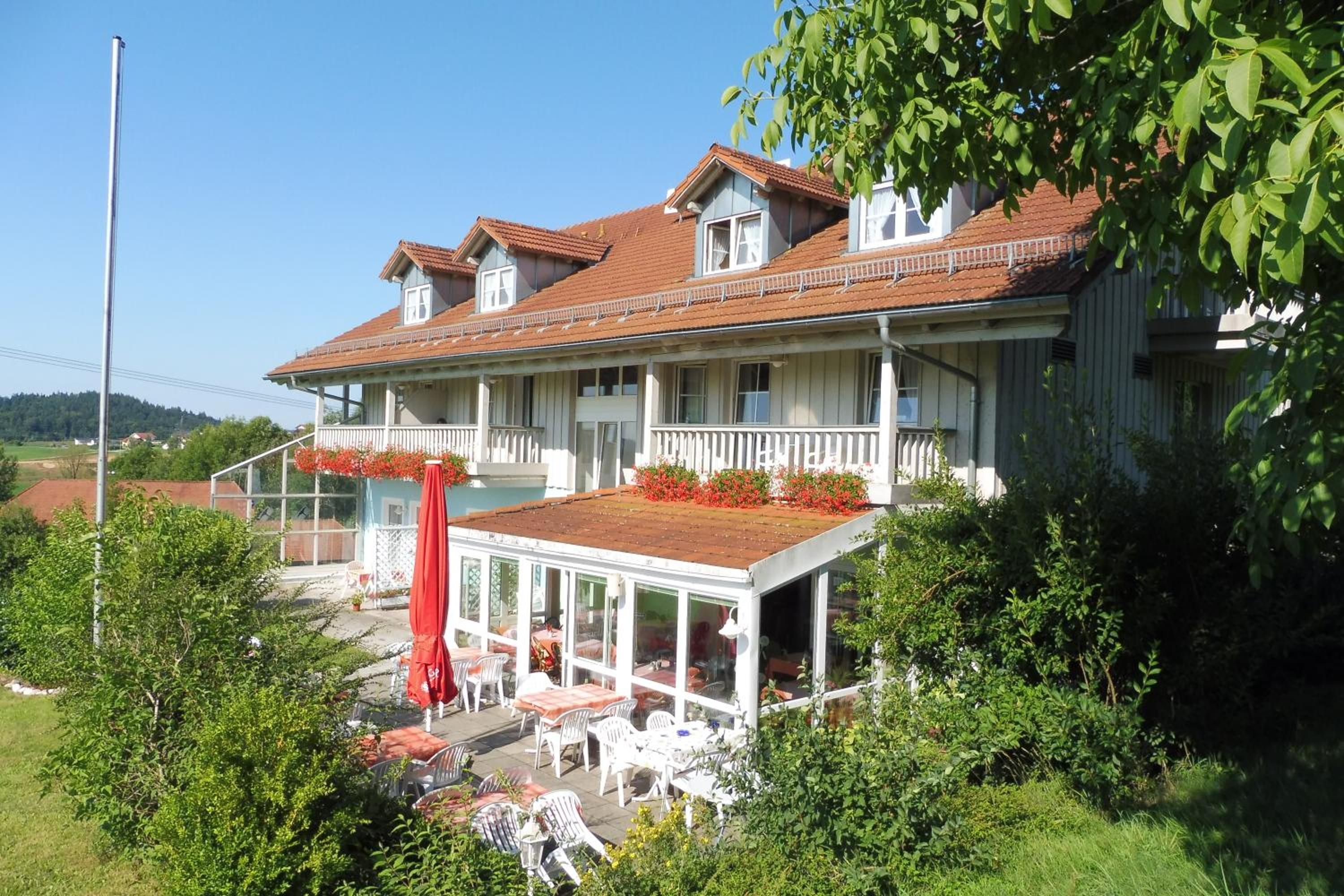 A two-story building with a balcony, outdoor seating area, and a red umbrella.