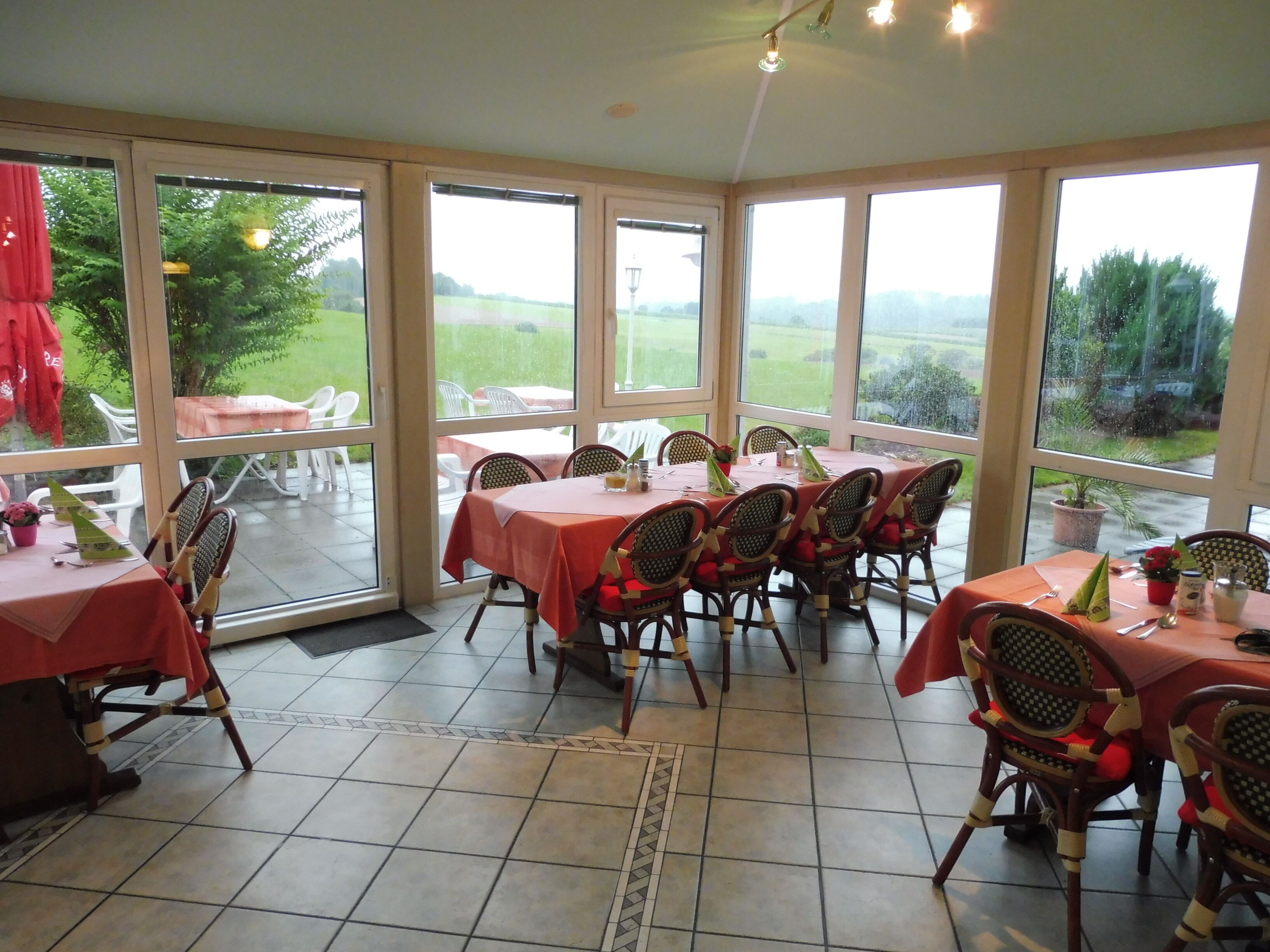 A sunroom with large windows, wicker chairs, and tables set for dining.