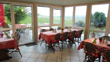A sunroom with large windows, wicker chairs, and tables set for dining.