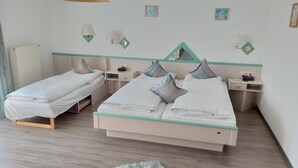 Una habitación de hotel con dos camas individuales, una cama grande, un felpudo mullido y lámparas fijadas a la pared.