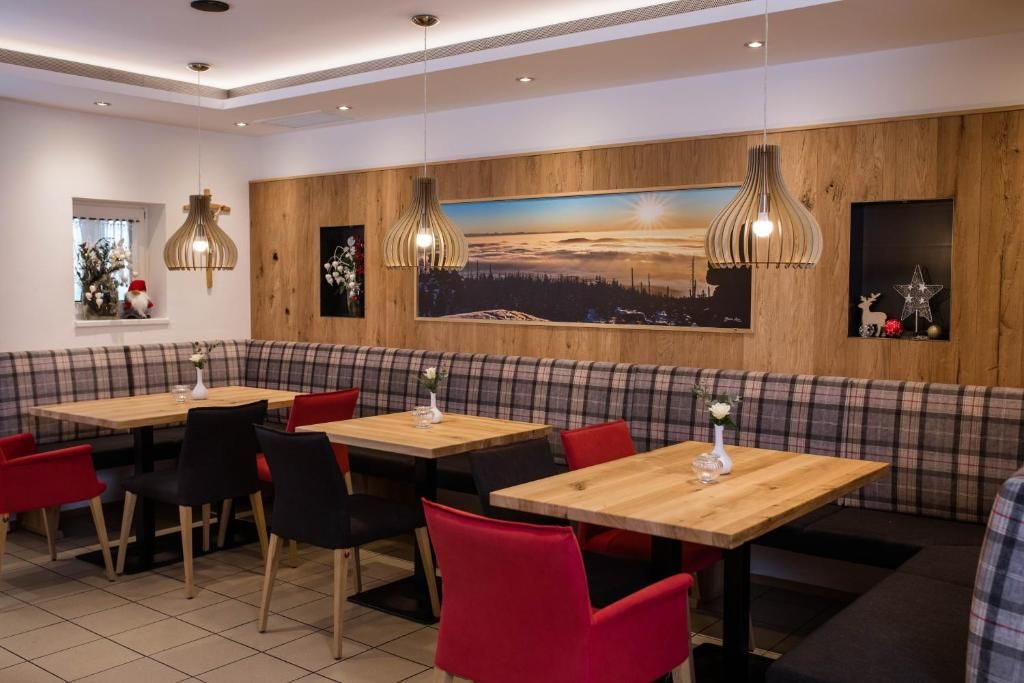 A restaurant with wooden panel walls, a large painting, and red and black chairs.