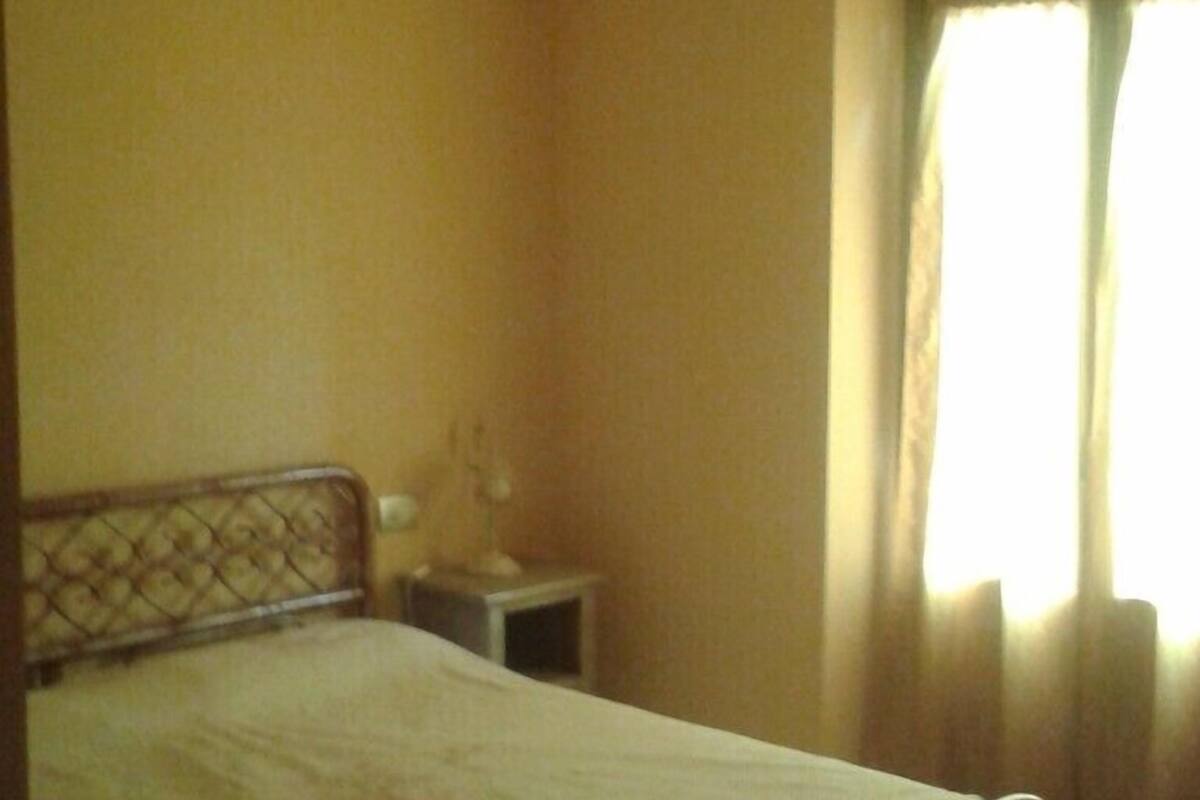 Ein Schlafzimmer mit Bett, Nachttisch, Lampe und einem Fenster mit Vorhängen.