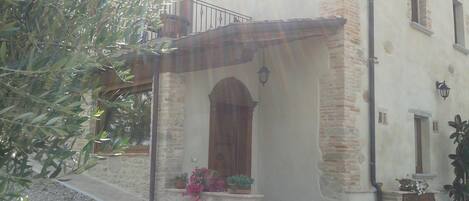 Un edificio con fachada de piedra, puerta de madera y un pequeño balcón con plantas en macetas.