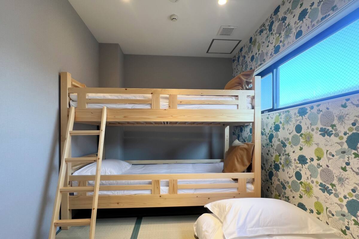 Una cama litera con escalera, una cama individual con almohada y una ventana con papel tapiz floral.