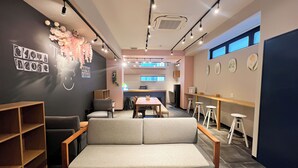 A modern cafe interior with a sofa, tables, and stools. - Hotel Hangout - Hostel (Osaka)