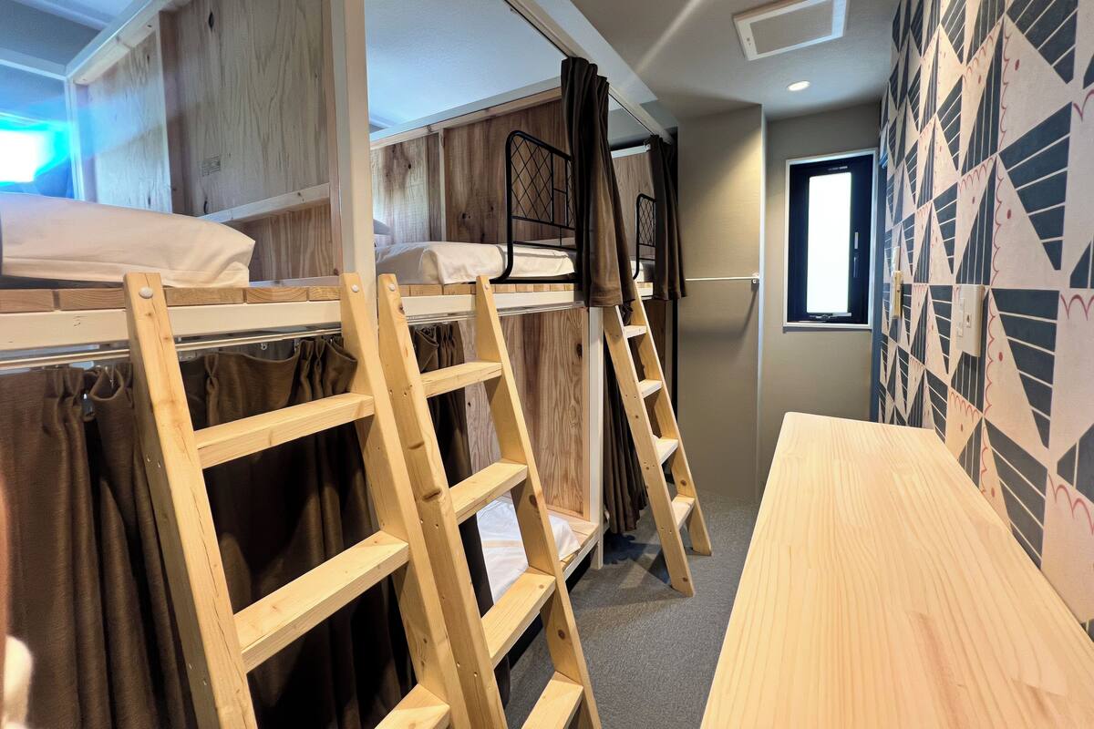 Dormitorio con literas, una escalera de madera y una mesita pequeña.