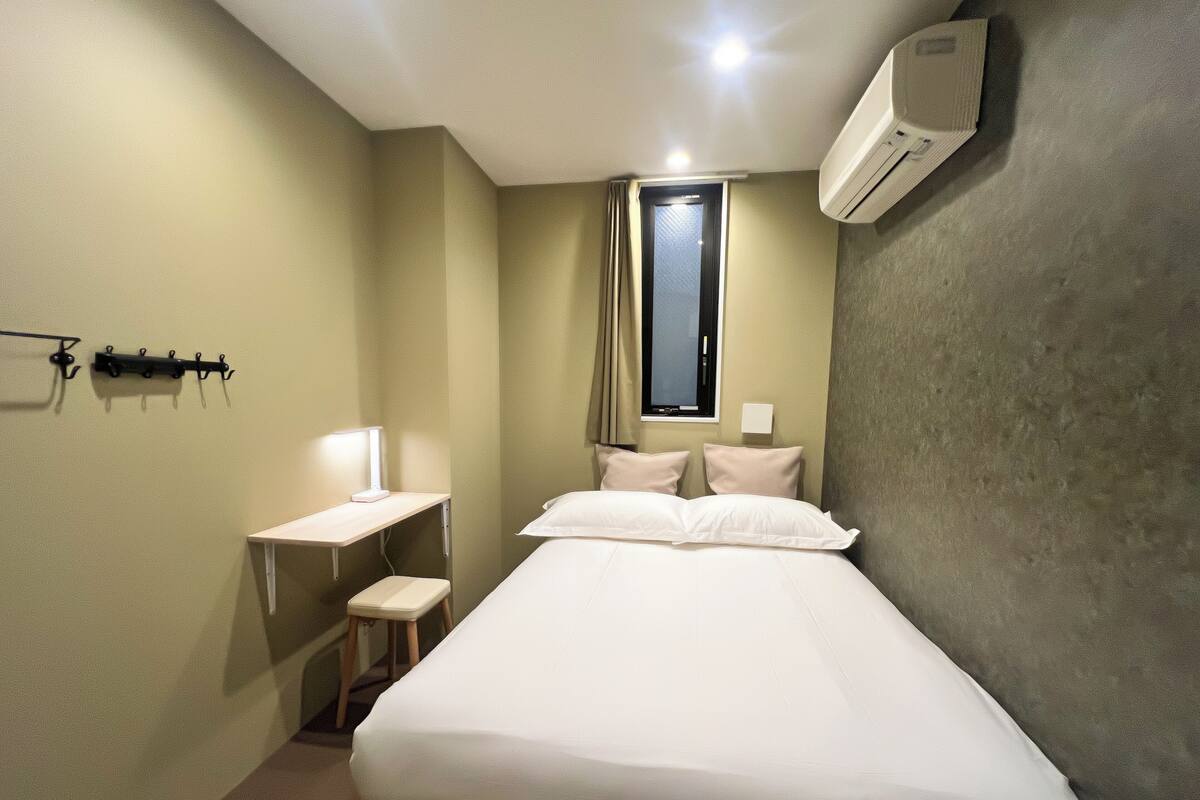 Una habitación de hotel con cama, escritorio, silla, ventana y aire acondicionado.