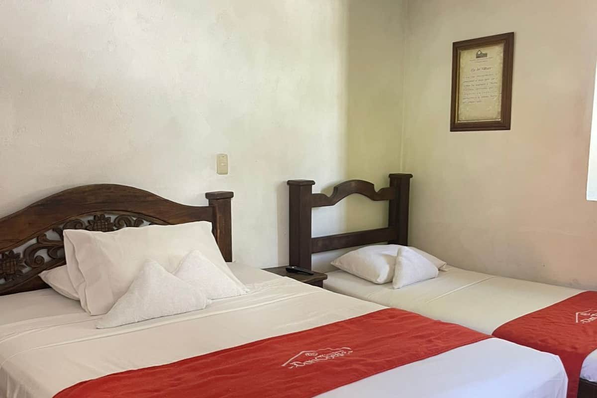 Un lit double avec une couvre-lit rouge, une tête de lit en bois et un certificat encadré accroché au mur.