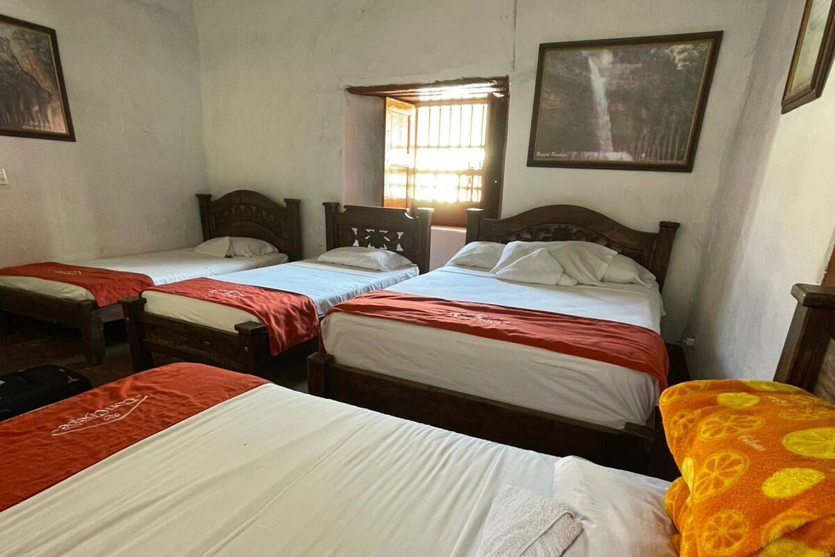 Une chambre avec trois lits simples, une fenêtre avec des barreaux et un tableau encadré au mur.
