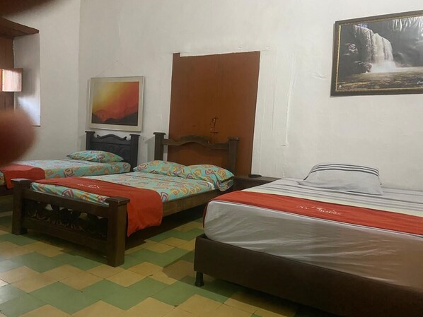 A room with two beds, a wooden headboard, a wooden door, and a framed picture on the wall.