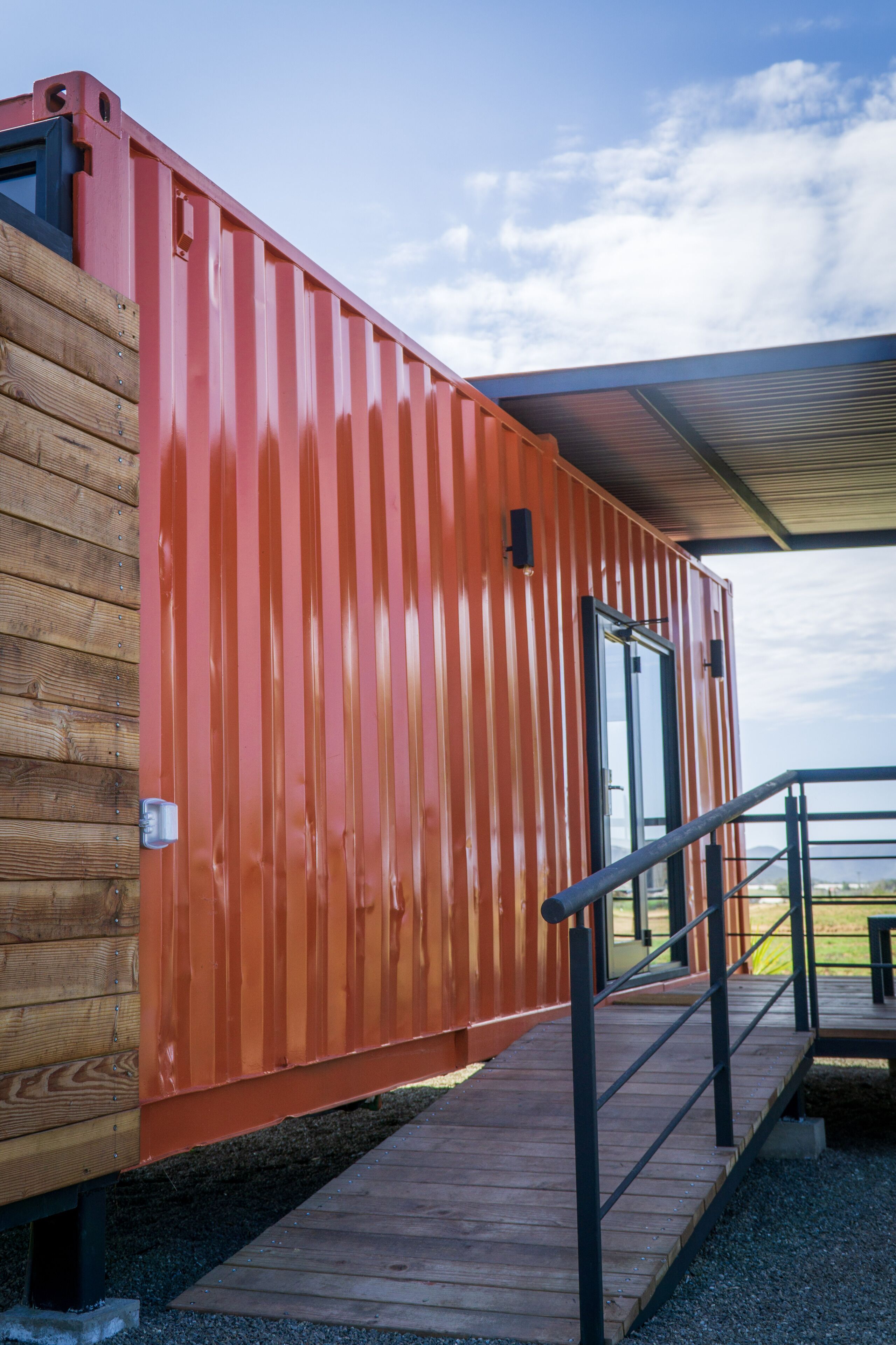 A red container-style building with a wooden deck and a metal railing.