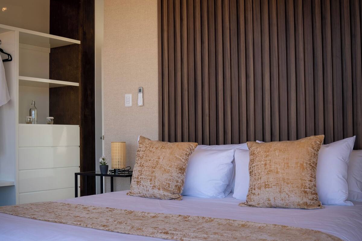 A modern hotel room with a large bed, a wooden headboard, and a white dresser.