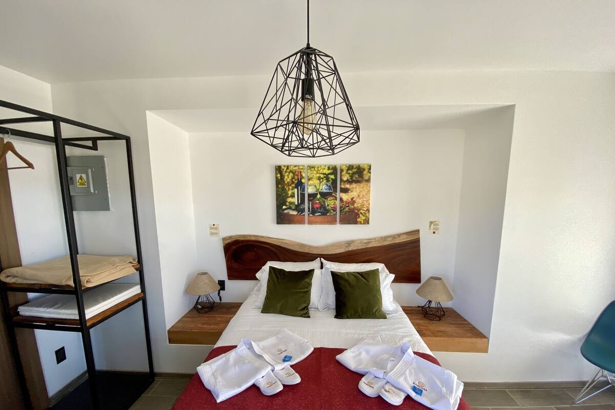 A hotel room with a bunk bed, a wooden headboard, a red bedspread, a wooden floor, and a hanging light fixture.