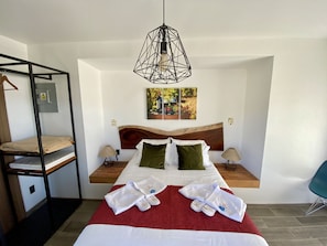 A hotel room with a bunk bed, a wooden headboard, a red bedspread, a wooden floor, and a hanging light fixture. - Xaroma (Valle de Guadalupe)
