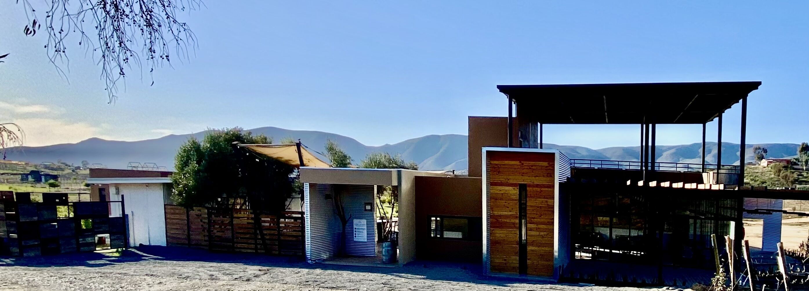 Un edificio moderno con techo plano y ventanas amplias, rodeado de montañas y un cielo despejado.