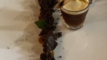 Een dessert op een wit bord, met een glas bruine vloeistof en een kaneelstokje.