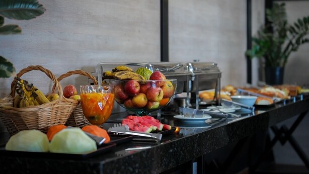 A buffet with various fruits, a glass of juice, and a basket of bread.