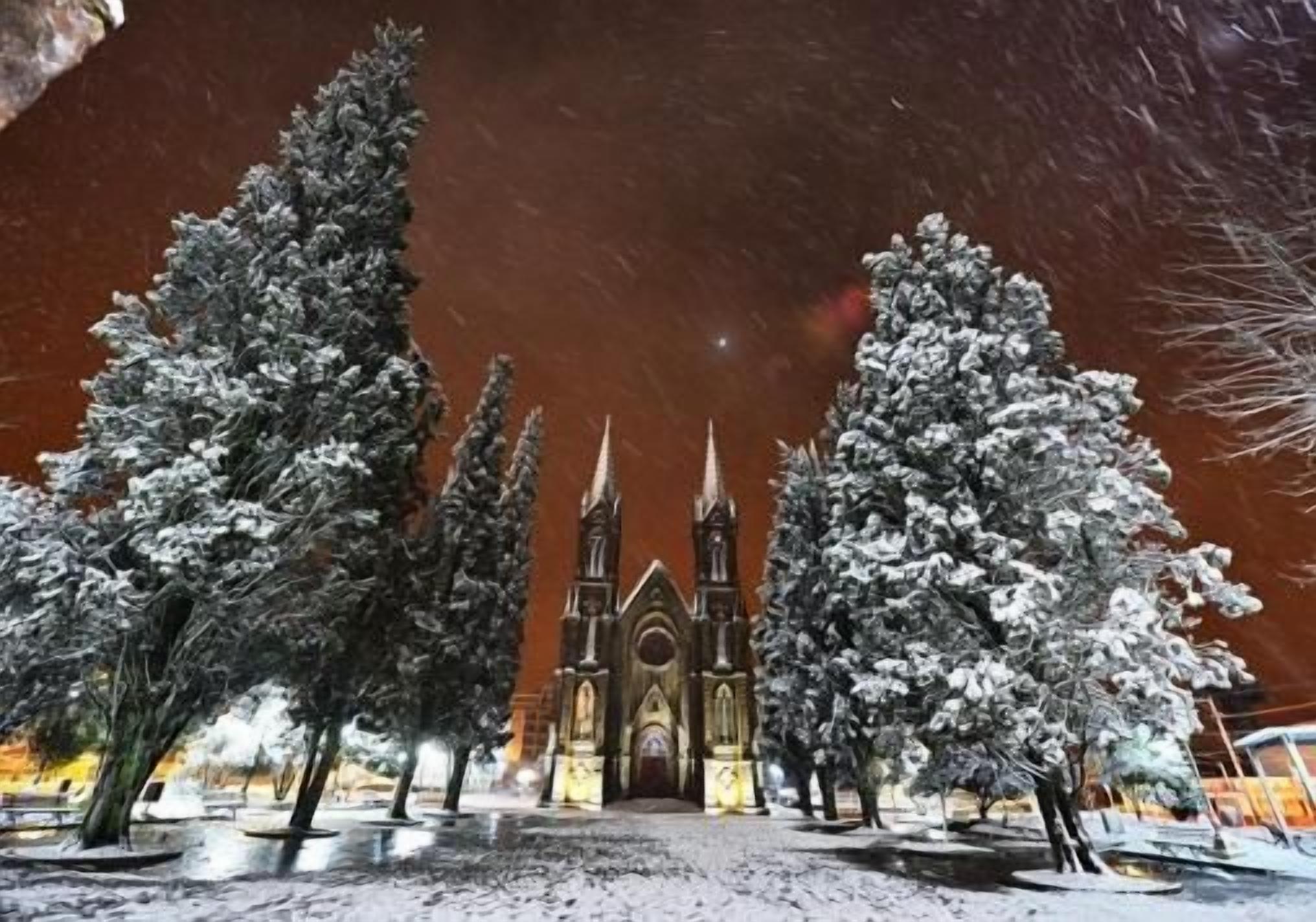 A snow-covered church with a gothic architectural style, surrounded by snow-laden trees.