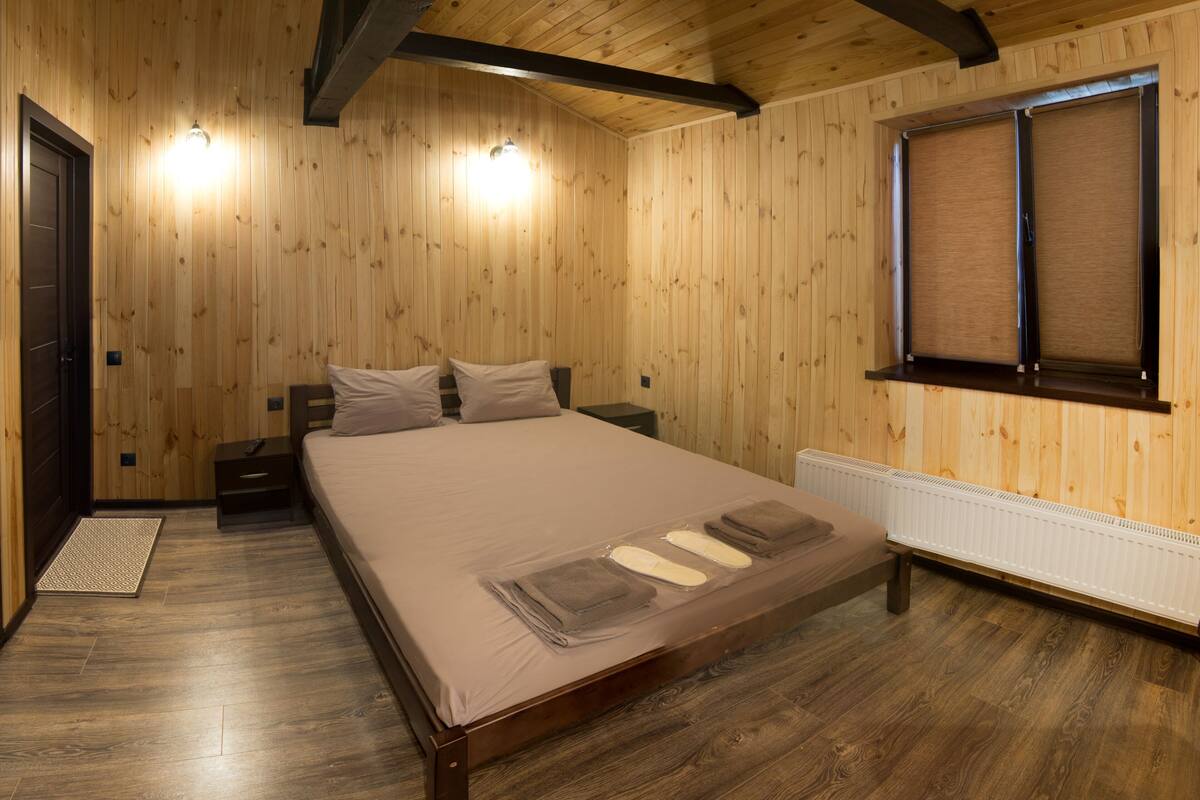 Ein Schlafzimmer mit Holzwänden, einem großen Bett, einem Heizkörper und einem Fenster mit Jalousien.