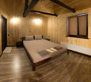 A wooden-paneled bedroom with a large bed, a radiator, and a window with blinds. - Sabi (Vita-Poshtova)