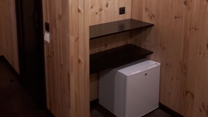 Quarto com paredes de painel de madeira, uma porta escura e um eletrodoméstico branco.