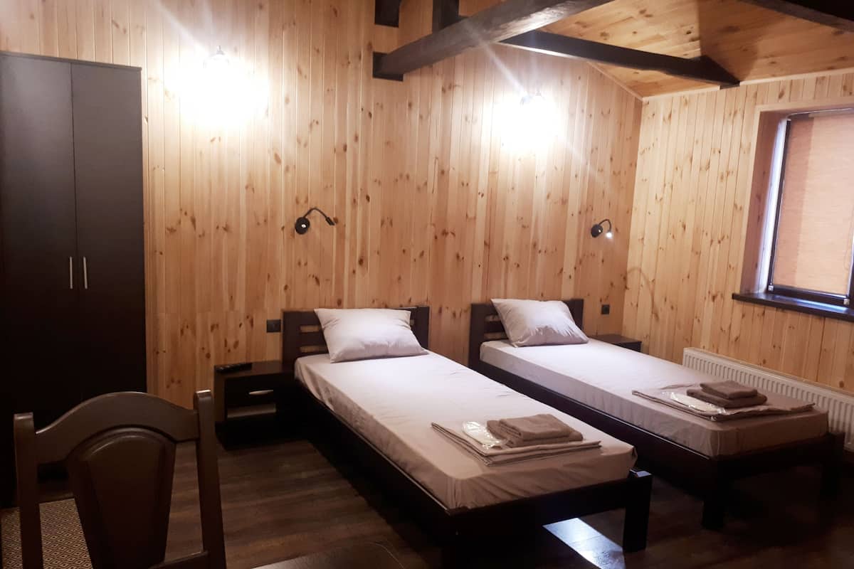 Ein Zimmer mit Holzwandverkleidung, zwei Einzelbetten, einem Schreibtisch und einem Stuhl.