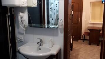 A bathroom with a white sink, a mirror, and a toilet. There is a clock on the wall and a TV in the corner.