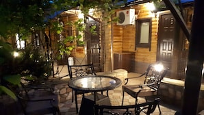 Um pátio com uma mesa redonda de vidro e quatro cadeiras, cercado por ladrilhos de pedra.