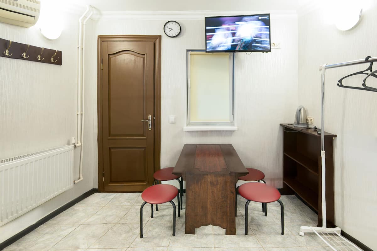 Ein Zimmer mit einem Holztisch, vier roten Stühlen, einem an der Wand montierten Fernseher, einer Tür und einem Heizkörper.