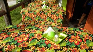 Una habitación con tres mesas cubiertas por coloridos manteles floreados, cada una con una bandeja verde y una servilleta blanca.