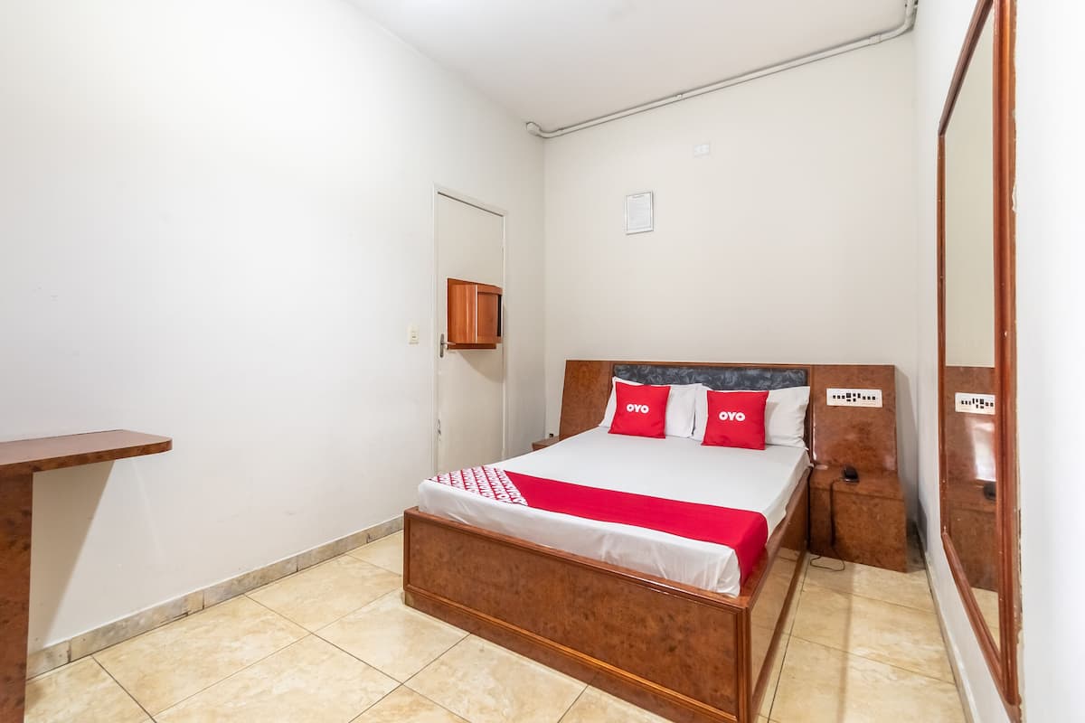 Een slaapkamer met een houten bed, een rood-wit dekbed en een klein nachtkastje.